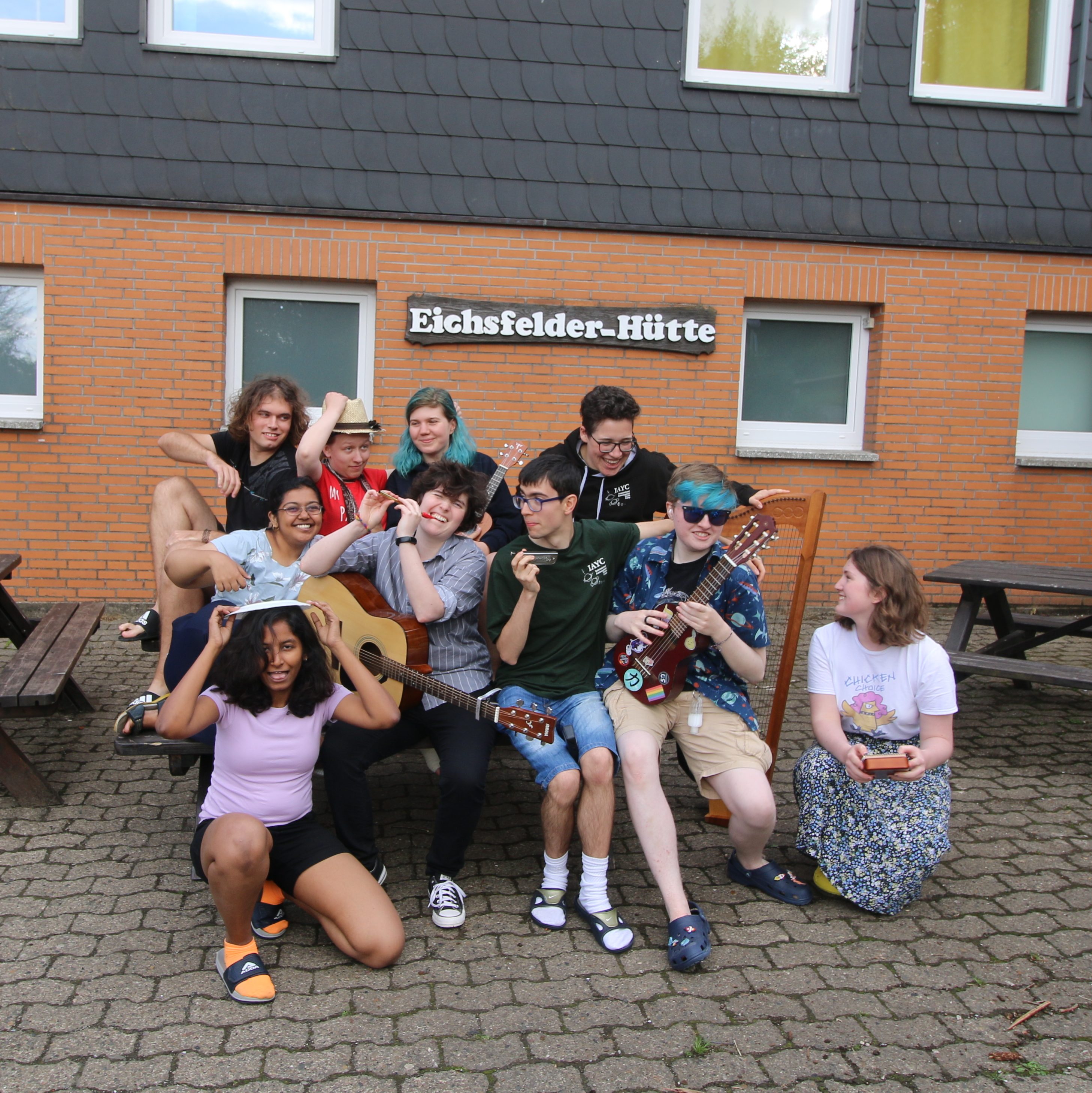 group of 10 young people posing in a silly manner with various musical instruments in front of a youth hostel