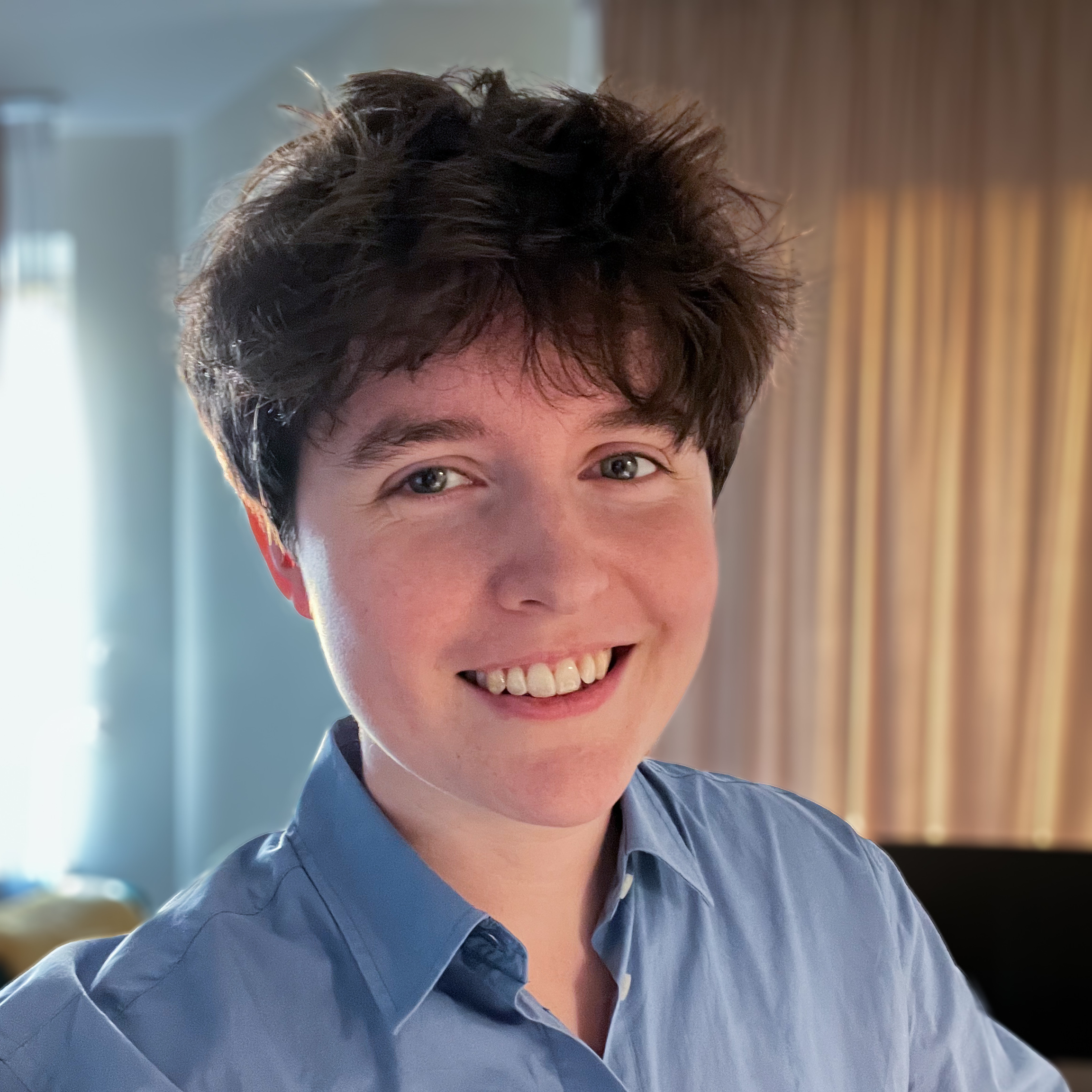 Selfie of me, a smiling white woman in a light blue smart buttoned shirt and very short brown hair.