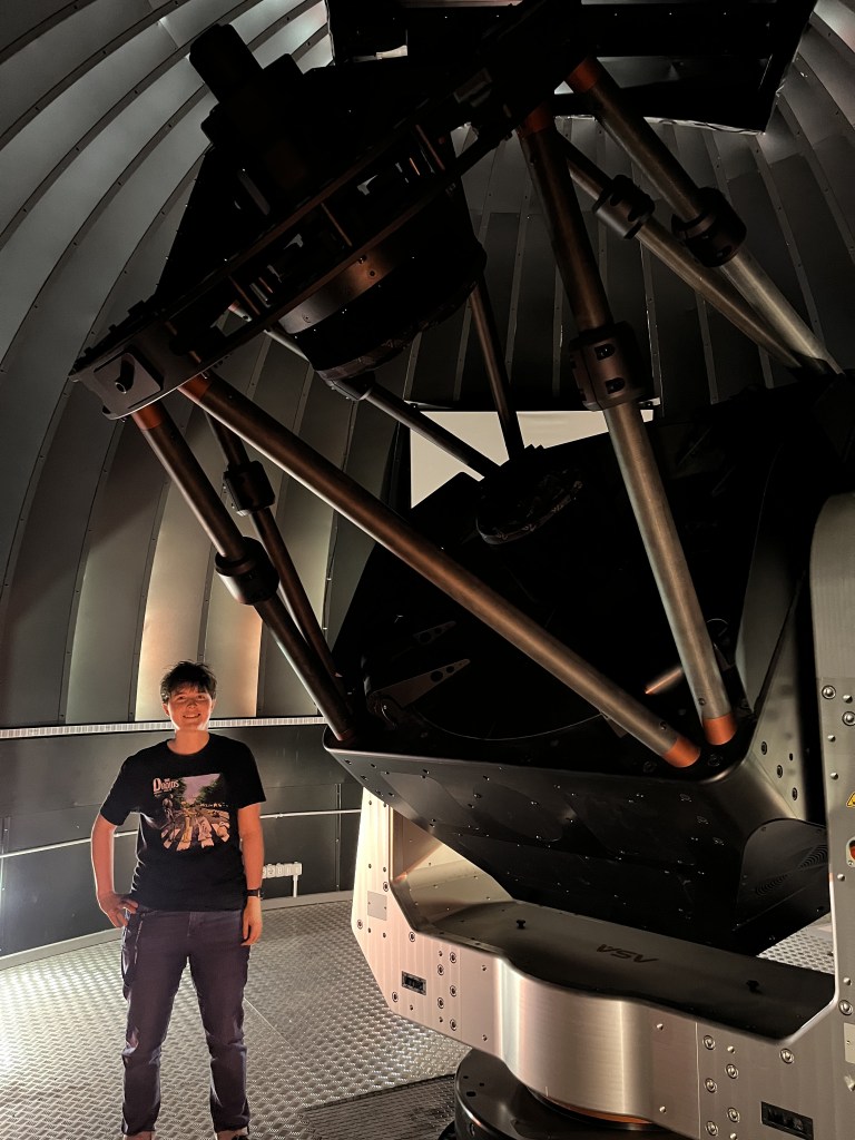 me standing next to a large telescope in a dome. the telescope mirror diameter of 1.5m is not much smaller than me at 1.65m