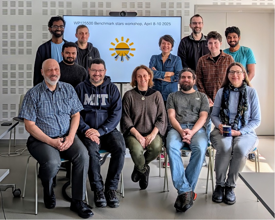a group of 12 people posing for a group picture in a university meeting room, with a tv that shows a cartoon sun logo for the benchmark stars group